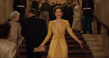 Movie still from “The Guernsey Literary and Potato Peel Pie Society” (2018), directed by Mike Newell – A woman in a yellow dress walking down a staircase; Medium shot, Low angle
