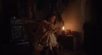 Movie still from “The Guernsey Literary and Potato Peel Pie Society” (2018), directed by Mike Newell – A woman sitting in a chair reading a book by a candle light; Medium shot, Low angle