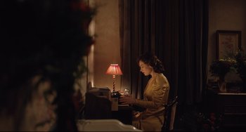 Movie still from “The Guernsey Literary and Potato Peel Pie Society” (2018), directed by Mike Newell – A woman sitting in front of a computer desk; Medium shot, High angle