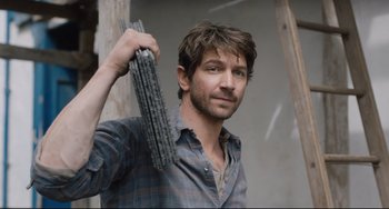 Movie still from “The Guernsey Literary and Potato Peel Pie Society” (2018), directed by Mike Newell – A man holding a bunch of metal rods in front of a wall; Close Up shot, Low angle