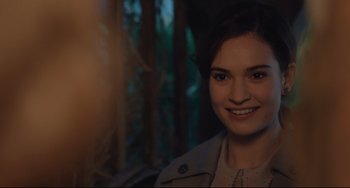 Movie still from “The Guernsey Literary and Potato Peel Pie Society” (2018), directed by Mike Newell – A woman smiling for the camera in front of trees; Close Up shot, Over the shoulder angle