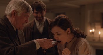 Movie still from “The Guernsey Literary and Potato Peel Pie Society” (2018), directed by Mike Newell – A man and a woman feeding a man a piece of food; Medium shot, Over the shoulder angle