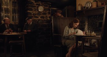 Movie still from “The Guernsey Literary and Potato Peel Pie Society” (2018), directed by Mike Newell – A woman sitting in a chair writing on a piece of paper; Medium shot, High angle