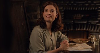 Movie still from “The Guernsey Literary and Potato Peel Pie Society” (2018), directed by Mike Newell – A woman sitting at a table with a book in front of her; Medium shot, Over the shoulder angle