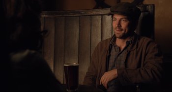 Movie still from “The Guernsey Literary and Potato Peel Pie Society” (2018), directed by Mike Newell – A man sitting at a table with a glass of beer in front of him; Medium shot, Over the shoulder angle