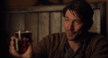 Movie still from “The Guernsey Literary and Potato Peel Pie Society” (2018), directed by Mike Newell – A person holding a drink in his hand; Close Up shot, Over the shoulder angle