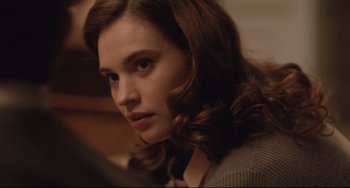 Movie still from “The Guernsey Literary and Potato Peel Pie Society” (2018), directed by Mike Newell – A woman with long brown curly hair stares into the distance; Close Up shot, Over the shoulder angle