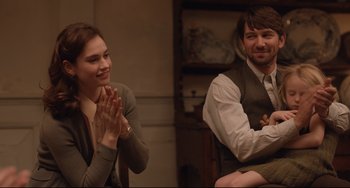 Movie still from “The Guernsey Literary and Potato Peel Pie Society” (2018), directed by Mike Newell – A woman clapping while a man sits next to her; Medium shot, Over the shoulder angle