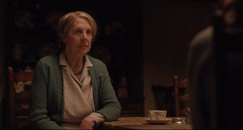 Movie still from “The Guernsey Literary and Potato Peel Pie Society” (2018), directed by Mike Newell – An older woman sitting at a table with a cup of coffee; Medium shot, Low angle