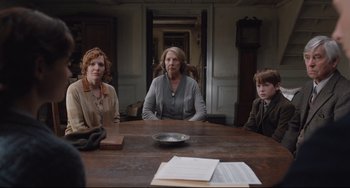 Movie still from “The Guernsey Literary and Potato Peel Pie Society” (2018), directed by Mike Newell – A group of people sitting at a wooden table; Medium shot, Over the shoulder angle
