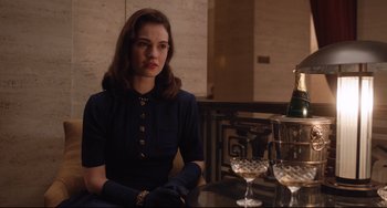 Movie still from “The Guernsey Literary and Potato Peel Pie Society” (2018), directed by Mike Newell – A woman sitting at a table with a glass of wine; Medium shot, Over the shoulder angle