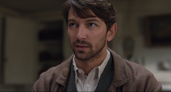 Movie still from “The Guernsey Literary and Potato Peel Pie Society” (2018), directed by Mike Newell – A person wearing a suit and tie; Close Up shot, Over the shoulder angle