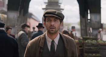 Movie still from “The Guernsey Literary and Potato Peel Pie Society” (2018), directed by Mike Newell – A man wearing a hat and a suit; Medium shot, Over the shoulder angle