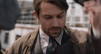 Movie still from “The Guernsey Literary and Potato Peel Pie Society” (2018), directed by Mike Newell – A person wearing a suit and tie; Close Up shot, Over the shoulder angle