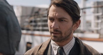 Movie still from “The Guernsey Literary and Potato Peel Pie Society” (2018), directed by Mike Newell – A person wearing a suit and tie; Close Up shot, Over the shoulder angle