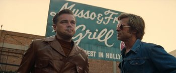 Movie still from “Once Upon a Time in Hollywood” (2019), directed by Quentin Tarantino – Two men standing next to each other in front of a sign for musso & frank grill; Medium shot, Low angle