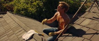 Movie still from “Once Upon a Time in Hollywood” (2019), directed by Quentin Tarantino – A man sitting on the ground smoking a cigarette and eating a banana peel; Medium shot, Low angle