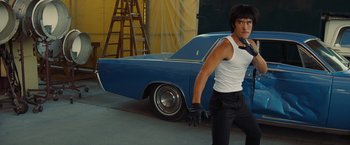 Movie still from “Once Upon a Time in Hollywood” (2019), directed by Quentin Tarantino – A young man standing in front of a blue car; Medium shot, Low angle