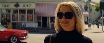 Movie still from “Once Upon a Time in Hollywood” (2019), directed by Quentin Tarantino – A woman wearing sunglasses standing in front of a store; Close Up shot, Low angle