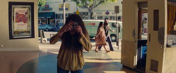 Movie still from “Once Upon a Time in Hollywood” (2019), directed by Quentin Tarantino – A woman taking a picture with a camera on the sidewalk; Wide shot, High angle