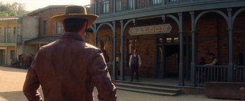 Movie still from “Once Upon a Time in Hollywood” (2019), directed by Quentin Tarantino – A man in a cowboy hat is standing in front of a saloon; Wide shot, Over the shoulder angle