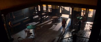 Movie still from “Once Upon a Time in Hollywood” (2019), directed by Quentin Tarantino – A man in a red shirt is standing in a room with tables; Wide shot, High angle