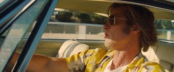 Movie still from “Once Upon a Time in Hollywood” (2019), directed by Quentin Tarantino – A man driving a car wearing sunglasses and a yellow shirt; Close Up shot, Low angle