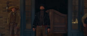 Movie still from “Once Upon a Time in Hollywood” (2019), directed by Quentin Tarantino – A man with a beard wearing a hat and holding a gun in his hand; Medium shot, Low angle