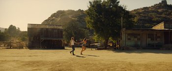 Movie still from “Once Upon a Time in Hollywood” (2019), directed by Quentin Tarantino – A man and a woman holding hands while running in the dirt; Extreme Wide shot, Low angle