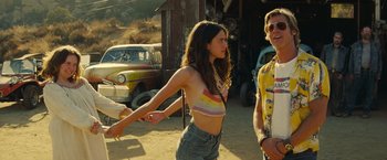 Movie still from “Once Upon a Time in Hollywood” (2019), directed by Quentin Tarantino – A man and a woman standing next to each other in front of an old car; Medium shot, Over the shoulder angle