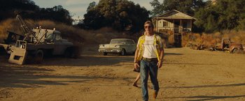 Movie still from “Once Upon a Time in Hollywood” (2019), directed by Quentin Tarantino – A man walking on a dirt road near a car; Wide shot, Low angle