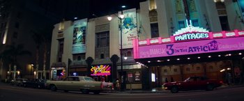 Movie still from “Once Upon a Time in Hollywood” (2019), directed by Quentin Tarantino – A car driving down a street next to a movie theater; Extreme Wide shot, High angle