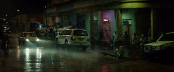 Movie still from “The Gunman” (2015), directed by Pierre Morel – A car driving down the street in the rain at night; Extreme Wide shot, High angle