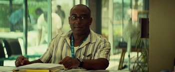Movie still from “The Gunman” (2015), directed by Pierre Morel – A man sitting at a table in front of a window; Close Up shot, Over the shoulder angle