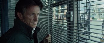 Movie still from “The Gunman” (2015), directed by Pierre Morel – A man holding a stick in front of a window; Close Up shot, Low angle