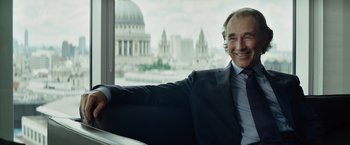 Movie still from “The Gunman” (2015), directed by Pierre Morel – A man in a suit and tie sitting in a chair; Medium shot, Over the shoulder angle