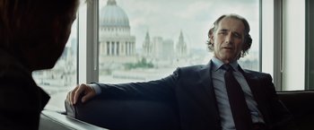 Movie still from “The Gunman” (2015), directed by Pierre Morel – A man in a suit sitting in front of a large window; Close Up shot, Low angle
