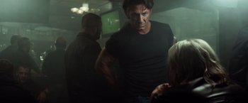 Movie still from “The Gunman” (2015), directed by Pierre Morel – A man standing in a room with another man and a woman; Medium shot, Over the shoulder angle