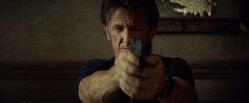 Movie still from “The Gunman” (2015), directed by Pierre Morel – A person holding a gun; Close Up shot, Low angle