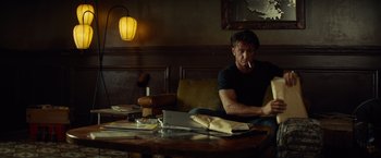 Movie still from “The Gunman” (2015), directed by Pierre Morel – A man sitting at a table with a cigarette in his mouth; Medium shot, Low angle