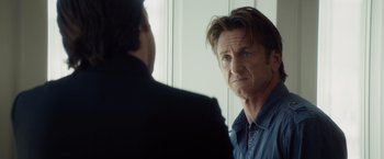 Movie still from “The Gunman” (2015), directed by Pierre Morel – A man looking at himself in the mirror while talking to another man; Close Up shot, Over the shoulder angle