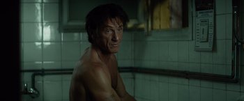 Movie still from “The Gunman” (2015), directed by Pierre Morel – A shirtless man sitting in a tiled bathroom; Close Up shot, High angle