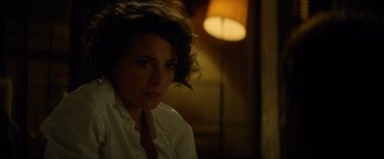Movie still from “The Gunman” (2015), directed by Pierre Morel – A woman in white shirt sitting in a dimly - lit room; Close Up shot, Over the shoulder angle