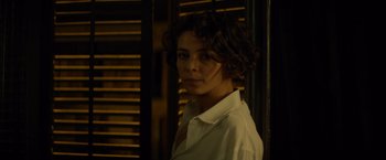 Movie still from “The Gunman” (2015), directed by Pierre Morel – A woman in a white shirt is standing by a window; Close Up shot, Over the shoulder angle