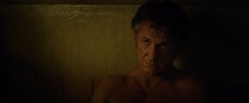 Movie still from “The Gunman” (2015), directed by Pierre Morel – A man with no shirt is sitting in a chair; Close Up shot, Over the shoulder angle