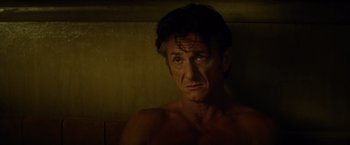 Movie still from “The Gunman” (2015), directed by Pierre Morel – A man with no shirt in a dark room; Close Up shot, Over the shoulder angle