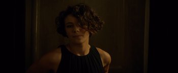 Movie still from “The Gunman” (2015), directed by Pierre Morel – A woman in a black dress is looking at the camera; Close Up shot, Over the shoulder angle