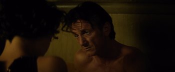 Movie still from “The Gunman” (2015), directed by Pierre Morel – A man with green eyes looking into a mirror; Close Up shot, Over the shoulder angle