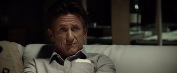 Movie still from “The Gunman” (2015), directed by Pierre Morel – A person sitting on a couch; Close Up shot, Over the shoulder angle