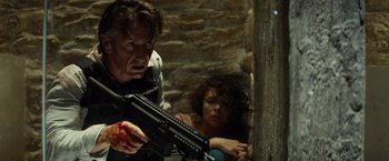 Movie still from “The Gunman” (2015), directed by Pierre Morel – A man holding a gun while a woman holds a gun; Medium shot, Low angle